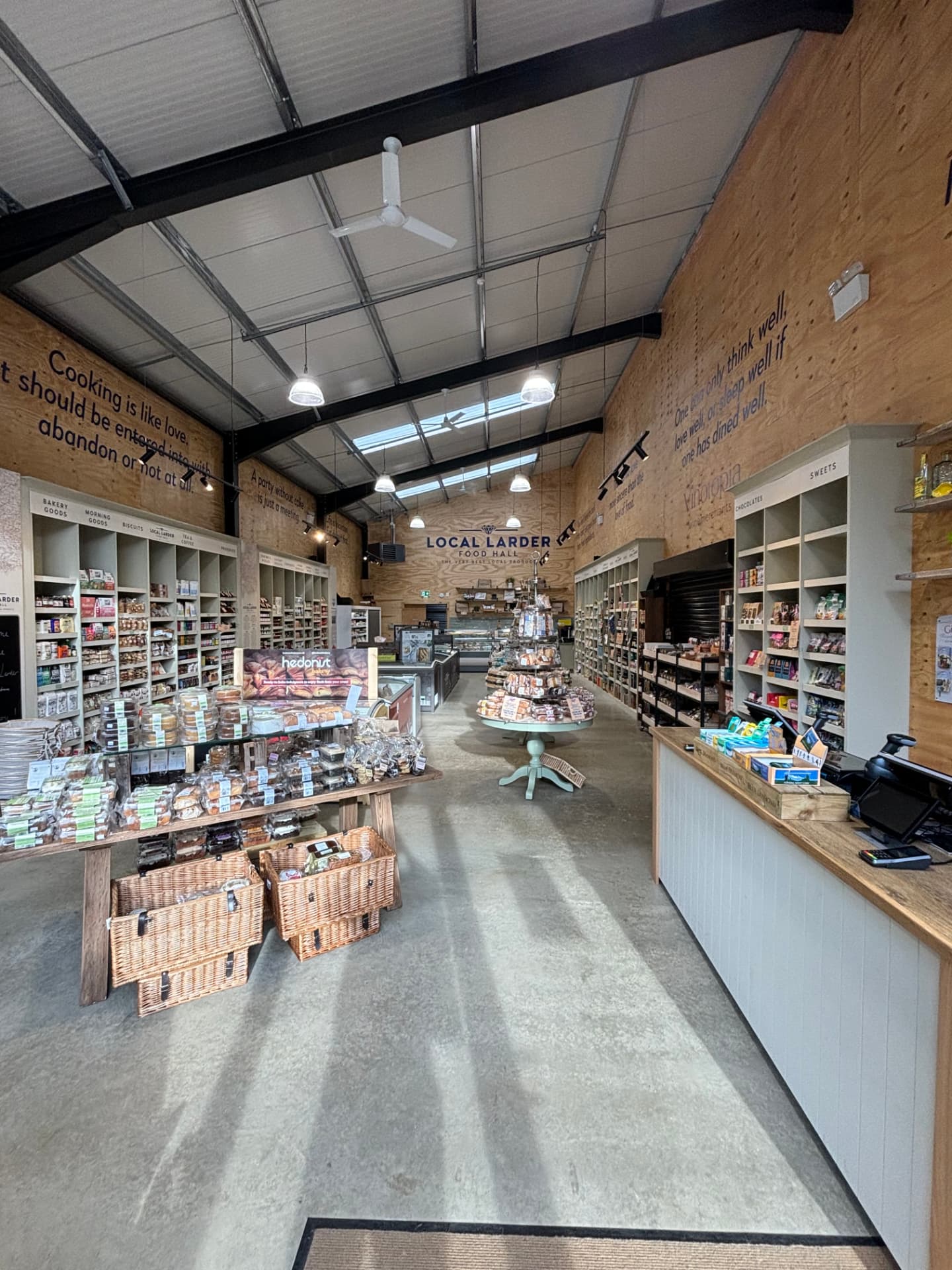Food hall retail interior with black track lighting above timber produce displays and wine shelving