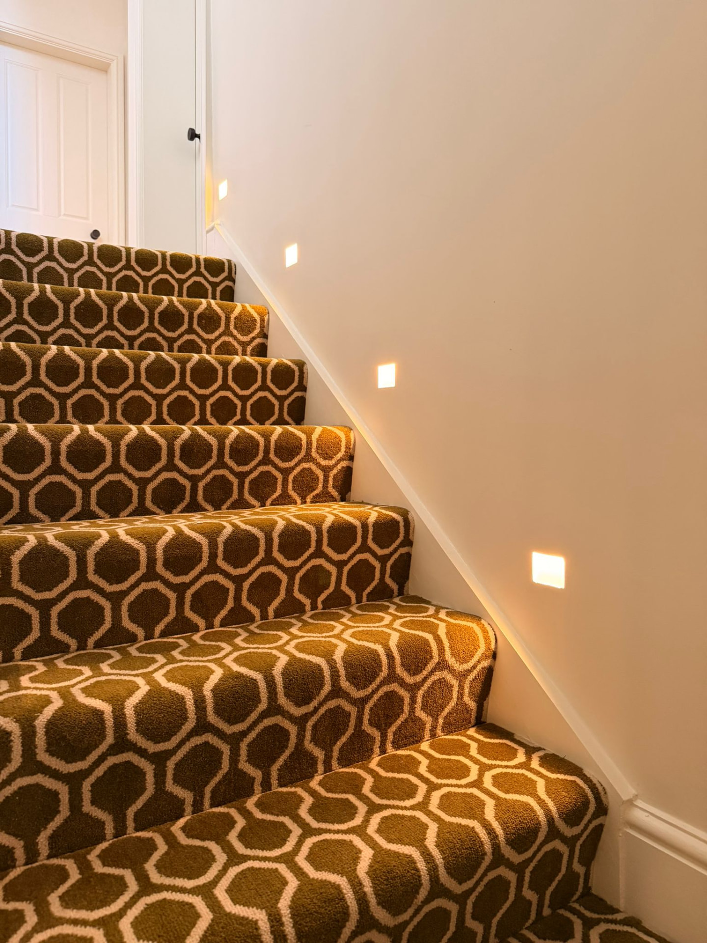 Staircase with patterned runner and recessed square wall lights