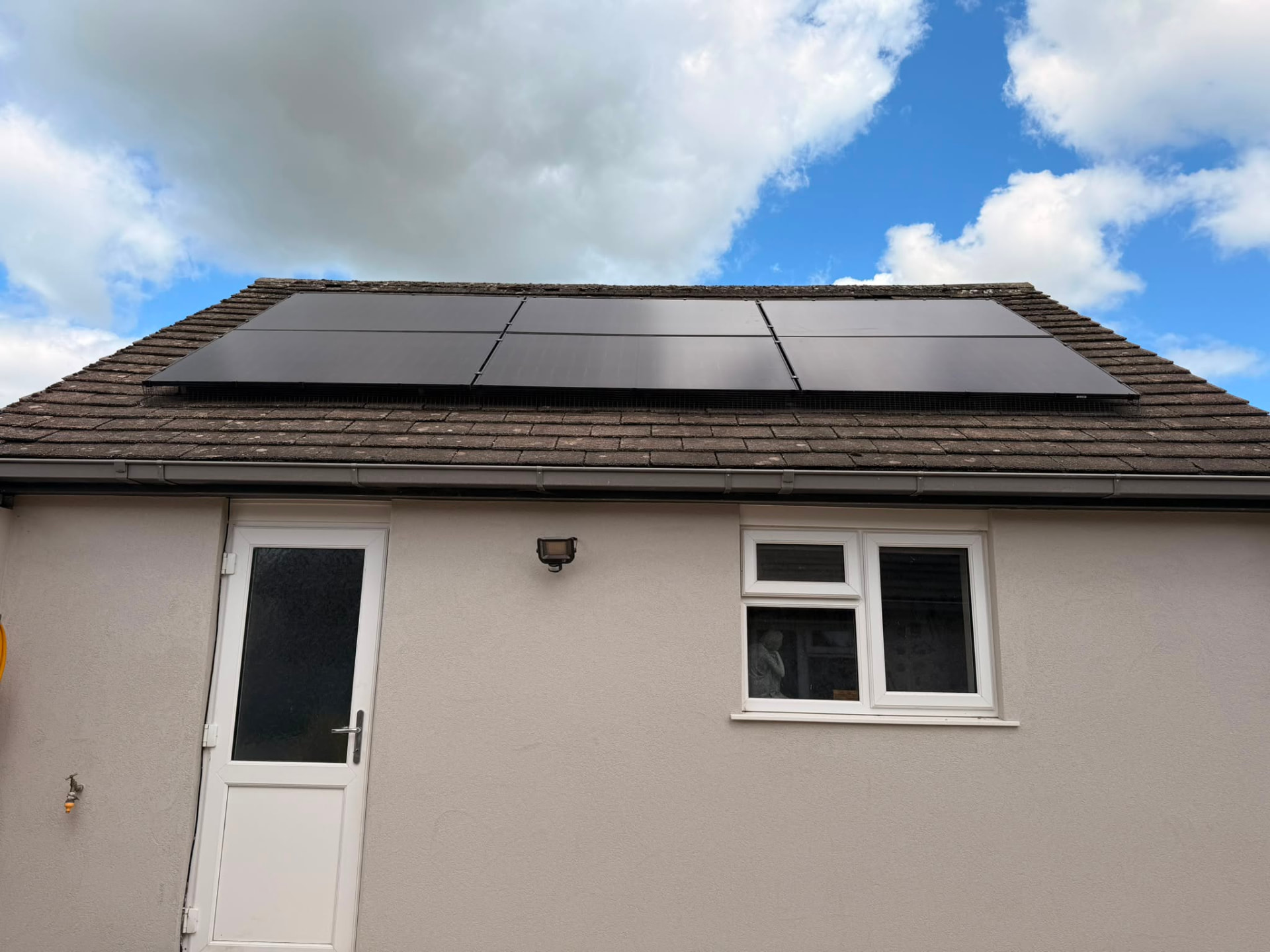 Black solar panels installed on a tiled garage roof under blue sky