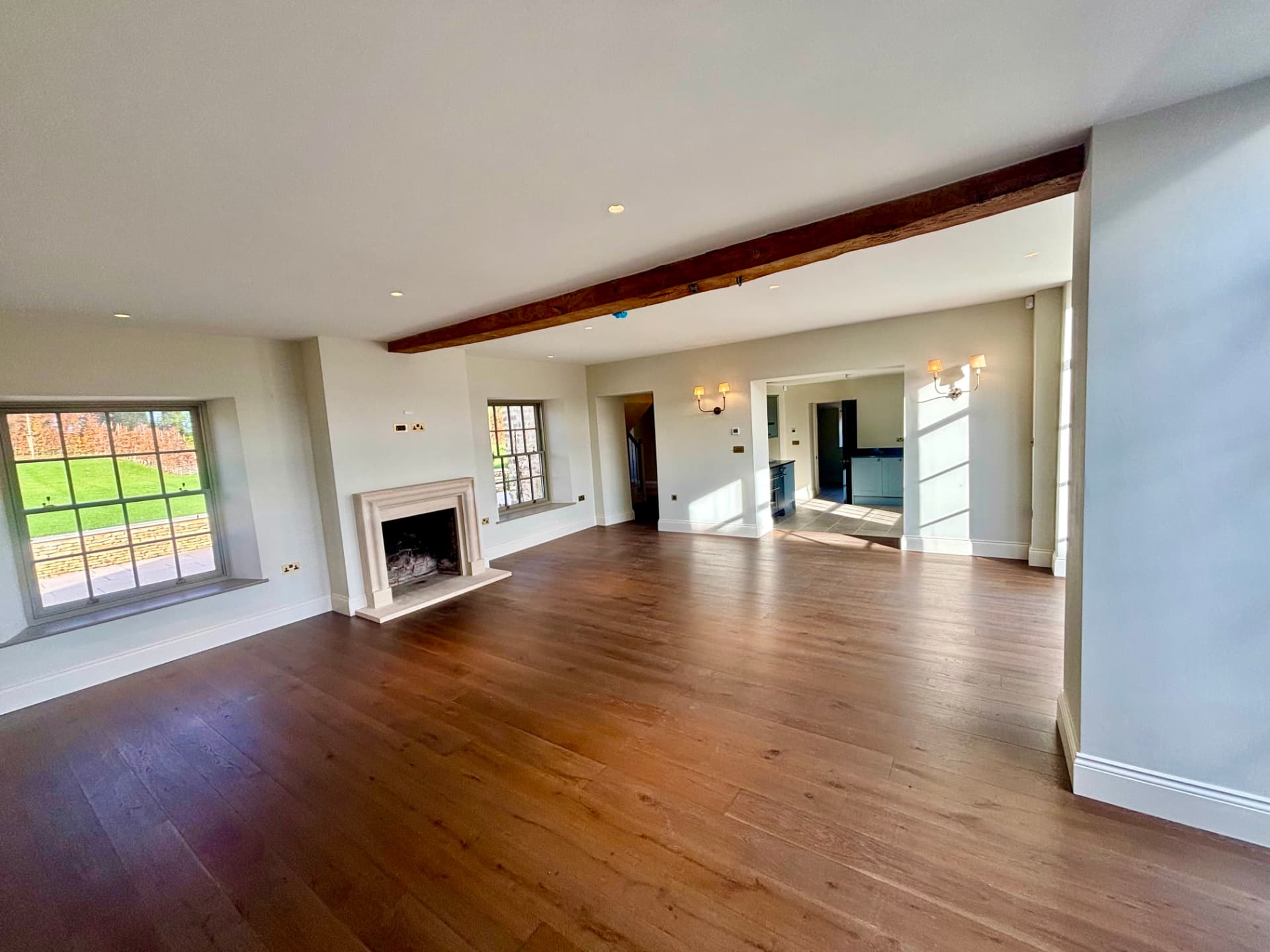 Sitting room with exposed beam fireplace, twin wall lights and discreet downlights in a converted Cotswold barn