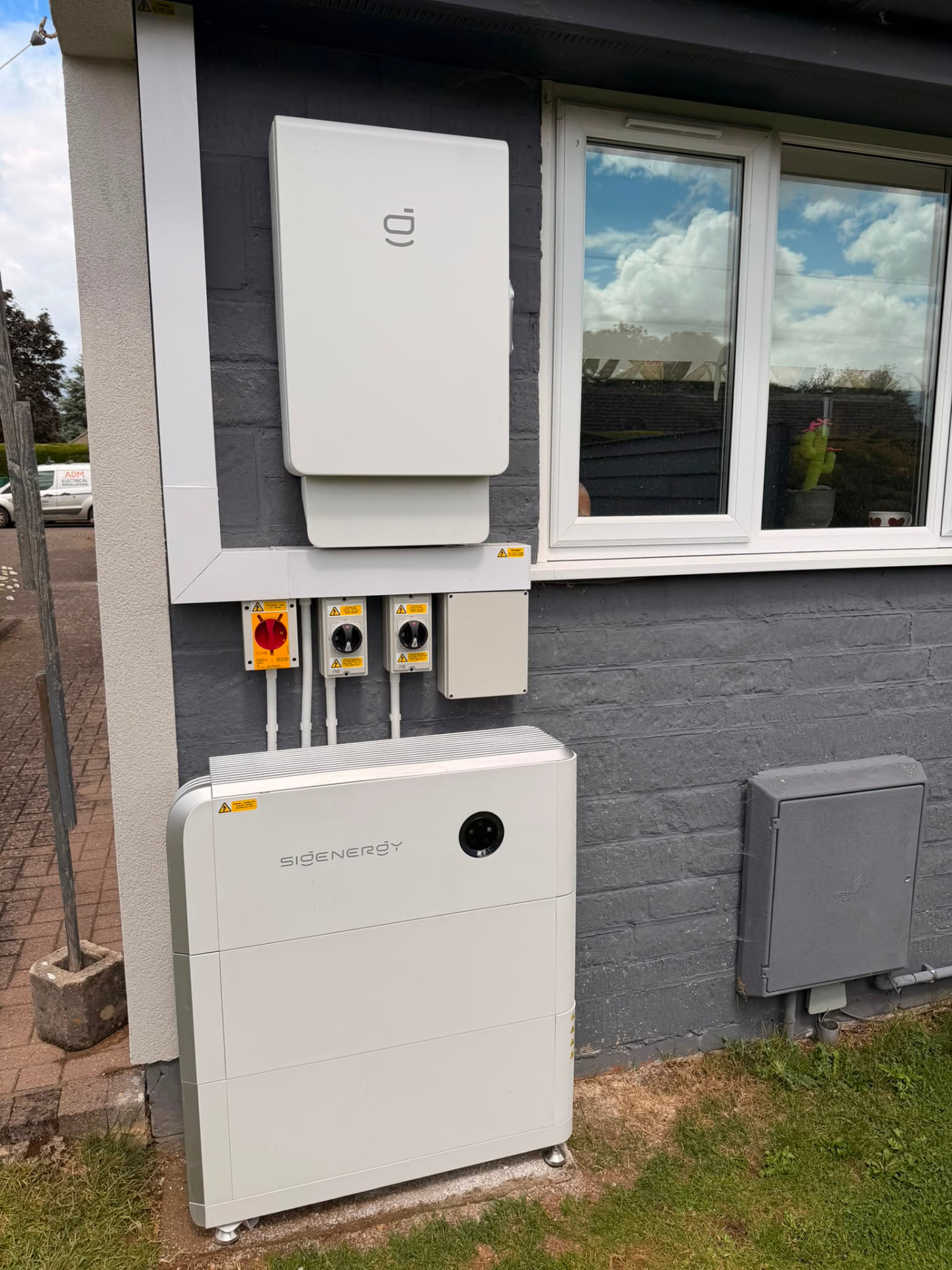 Solar panels on the roof of a Cotswold stone house with a modular battery storage cabinet beside the wall