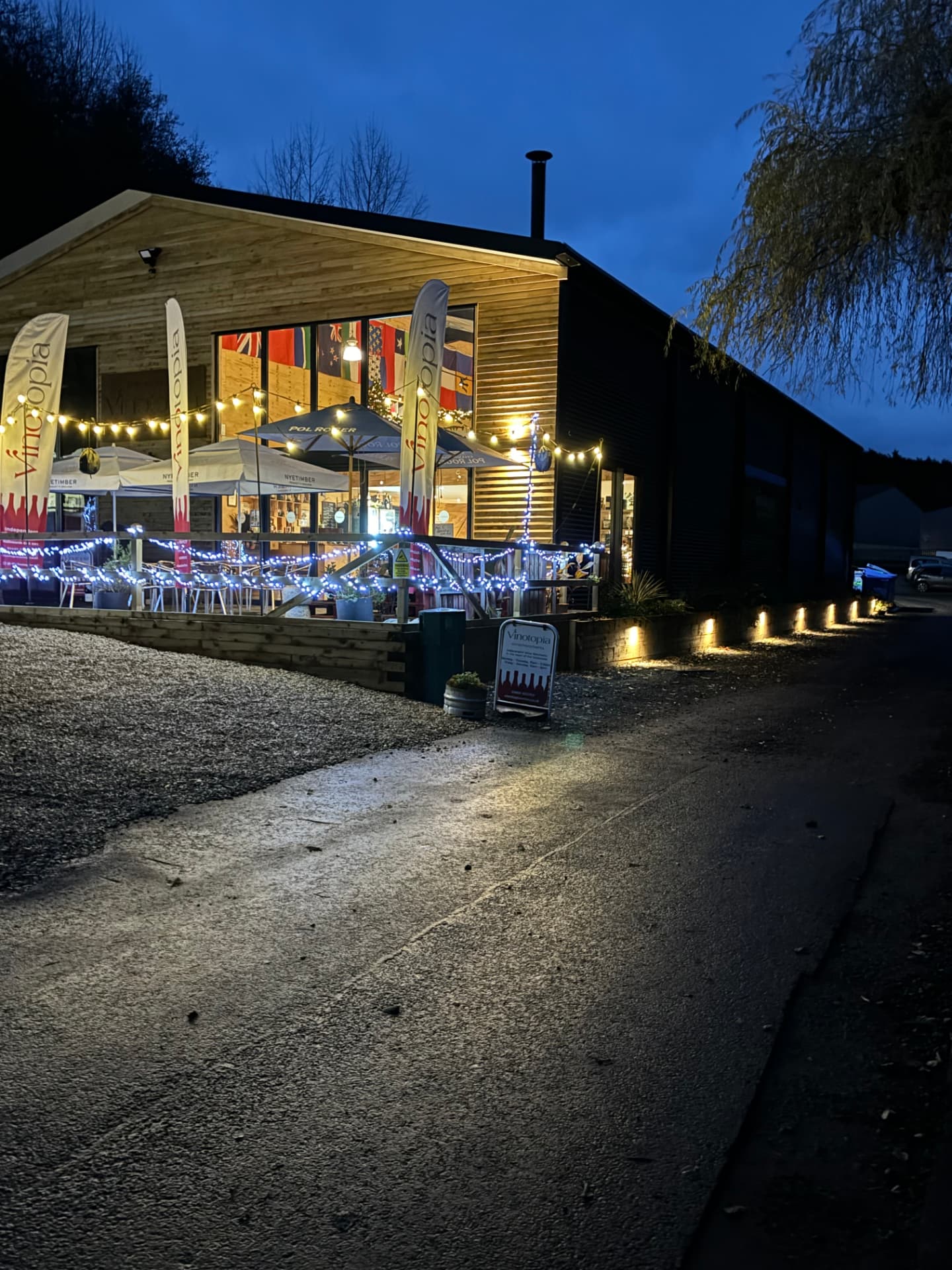 Timber-clad retail building lit at dusk with festoon and wall-wash lighting